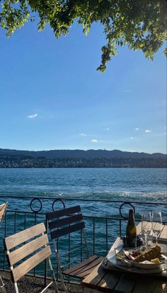 two chairs and a table with food on it near the water