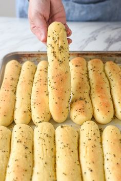 someone is holding a piece of bread in the middle of a baking pan filled with garlic breadsticks