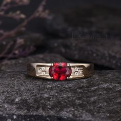 a close up of a ring with a red stone in the middle on a rock