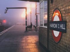 a person sitting on a bench next to a train station with fog in the air