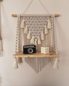 a wall hanging with some tassels and a camera on the shelf next to it