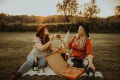 two women sitting on a blanket eating pizza and drinking sodas while the sun is setting