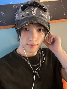 a young man with headphones on his ears wearing a black shirt and baseball cap