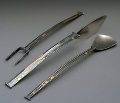 three silver serving utensils and spoons on a gray surface