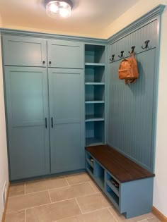 a room with blue cabinets and a bench in the center, two bags hanging from hooks on the wall