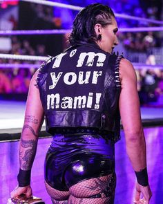 a woman with tattoos on her back walking in a wrestling ring wearing a leather vest that says i am your mama