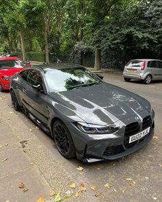 a grey sports car parked on the side of a road next to other cars and trees