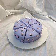 a purple cake with pink flowers on it sits on a white plate and is ready to be cut into pieces