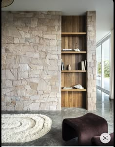 a living room with a stone wall and bookcase next to a large glass window