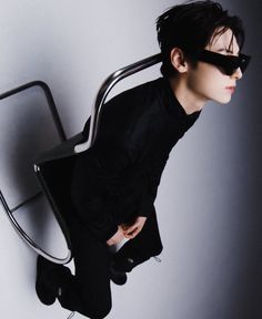 a man sitting on top of a metal chair with his hands in his pockets and wearing sunglasses