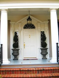 a white door with two large planters on the front steps and an entry way