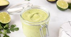 an avocado smoothie in a glass jar with limes and cilantro on the side