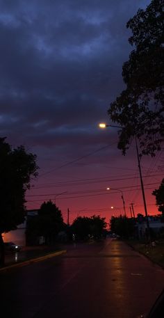 an empty street at night with the sun setting in the distance and trees lining the road