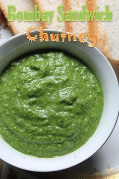 a white bowl filled with green soup next to slices of bread