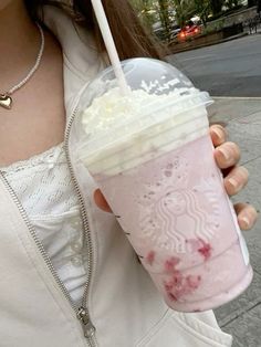 a woman holding up a pink drink with strawberries in it's cup while standing on the sidewalk