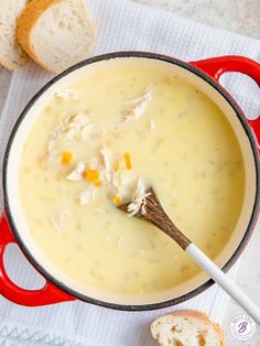 a red pot filled with chicken and cheese soup next to bread on a white towel