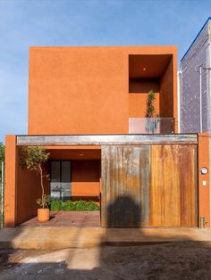 an orange building with a metal door and planter in the front yard, on a sunny day