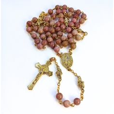 Miraculous Medal Rosary Rhodonite beads with gold bead caps. This beautiful, handcrafted Catholic Heirloom Rosary combines 6mm Rhodonite beads with a Miraculous Medal centerpiece in a gold finish and a gold finish Saint Benedict Crucifix. The Pater beads are 6mm Rhodonite beads with gold finish bead caps. Dimensions & Specifications: Ave Beads: 6mm Rhodonite beads. Pater Beads: 6mm Rhodonite beads with gold finish bead caps Crucifix: The gold finish Saint Benedict Crucifix measures 1-1/2 Inches H. Center: The Miraculous Medal centerpiece in a gold finish measures 1-3/4 inch H. Length: The filigree rosary measures 20.5" long. Wire: 20-gauge 18 k gold plated wire A gift for prayer and devotion. Comes in a gift box with a instructional prayer card on How to Pray the Rosary. * This rosary woul Gold Rosary With Gemstone Beads Gift, Gold Spiritual Rosary With Gemstone Beads, Gold Gemstone Beads Rosary, Gold Rosary With 8mm Beads For Healing, Gold Hand-strung Spiritual Rosary, Handmade Gold Rosary For Healing, Handmade Gold Healing Rosary, Gold Bohemian Rosary With 8mm Beads, Bohemian Gold Rosary With 8mm Beads