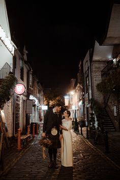 a bride and groom are walking down the street at night in an old european town