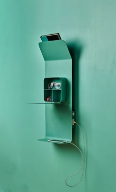 a green wall mounted with a pair of glasses in it's holder and wires