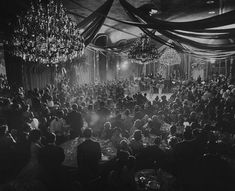 an old black and white photo of people in a banquet hall with chandeliers hanging from the ceiling