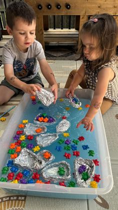 two children playing with plastic beads in a tray on the floor next to a table