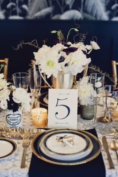 the table is set with white flowers and gold place settings for an elegant wedding reception