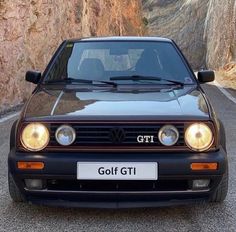 a black golf gti parked on the side of a road next to a cliff