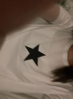 a baby laying on top of a bed wearing a white shirt with a black star on it