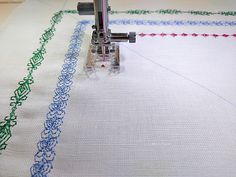 an embroidery machine is working on a white piece of fabric with blue and green stitching