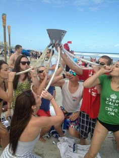 a group of people standing on top of a beach next to the ocean holding up large objects