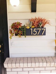 a house number sign with succulents and other plants on the front porch