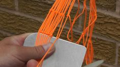 someone is holding an orange string in front of a brick wall that has been made into a sculpture