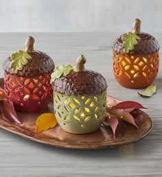 three decorative pumpkins sitting on top of a wooden platter with leaves and candles