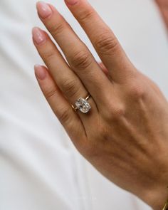 a woman's hand with a diamond ring on her left hand, wearing a white shirt