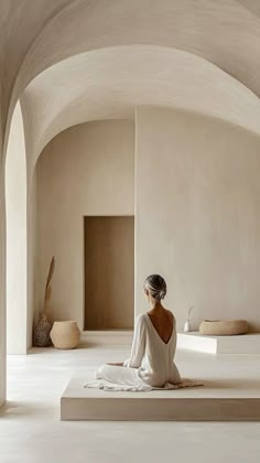 a woman is sitting on the floor in a room with white walls and arches around her