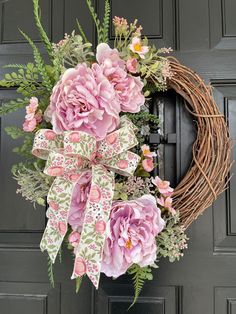 a wreath with pink flowers and green leaves on the front door is adorned with ribbon