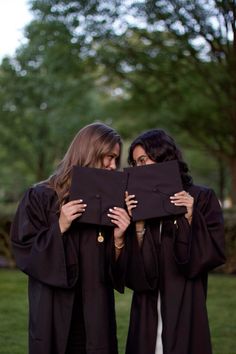 two women in graduation gowns are holding up a black piece of cloth that they have been placed on