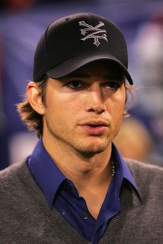 a man wearing a baseball cap and blue shirt looks off to the side as he stands in front of an audience