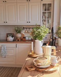 a kitchen with white cupboards and wooden table in front of the window, surrounded by potted plants