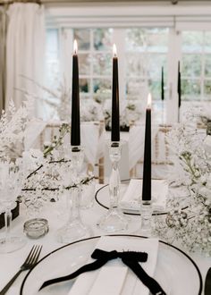 the table is set with black and white place settings, candles, and flowers in glass vases