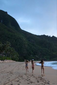 three girls are running on the beach with their arms in the air and one girl is throwing a frisbee