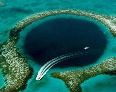 an aerial view of a blue hole in the ocean with two boats passing by it