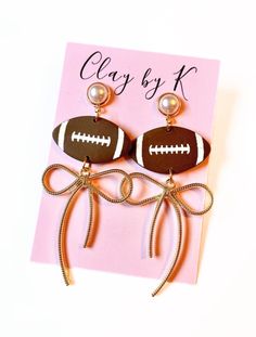 a pair of brown and white football earrings with pearls on them sitting next to a pink card