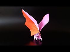 an origami bird on a black surface with red and orange wings, in the dark