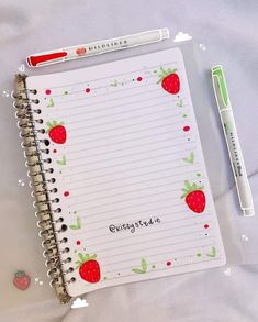 a notebook with strawberries on it next to a pen