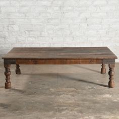 an old wooden table sitting in front of a white brick wall with no one around it