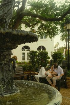 a man and woman sitting on a bench next to a fountain