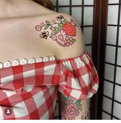 a woman wearing a red and white checkered shirt has a strawberry tattoo on her shoulder