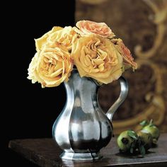 a silver vase filled with yellow flowers on top of a table